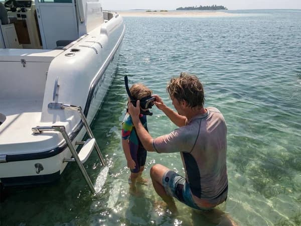 Crew member fitting a snorkel mask on a young child in shallow water